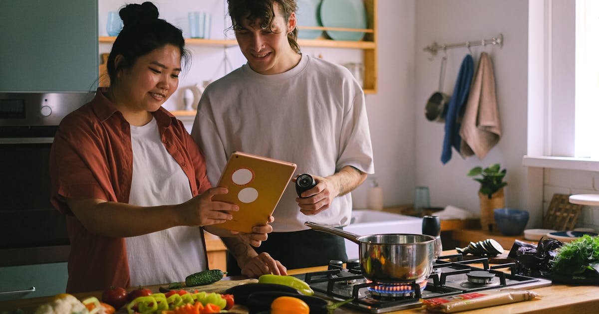 Thermomix on a kitchen worktop next to a tablet showing the Cookidoo app and a handwritten weekly meal plan