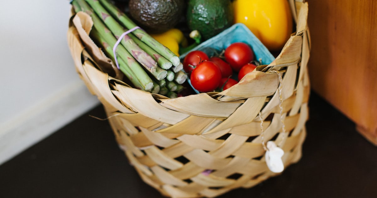 Well-organised shopping list on a wooden kitchen counter next to fresh vegetables and a pen