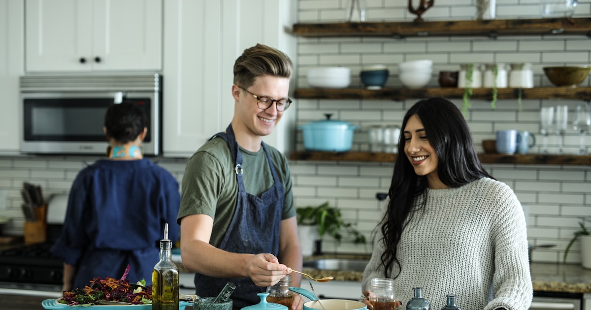 Mother and child cooking together in a bright kitchen, the child stirring a pot and laughing
