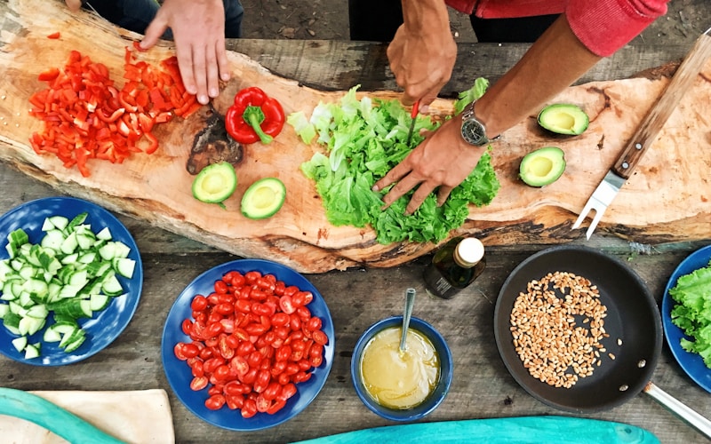 Zwei Kinder rollen gemeinsam Pizzateig aus, Mehl auf den Händen und auf der Arbeitsfläche