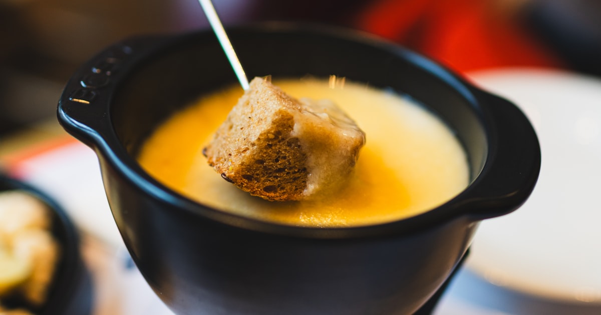 Raclette table set with melted cheese, potatoes, cornichons, and colourful vegetables